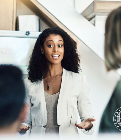 Project Manager giving explanation to her team, professional setting, The Prime College